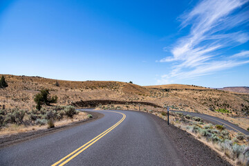 Winding road in a dry, desert with blue skies and sage brush, representing the American West and scenic road trips. Maupin, Oregon.