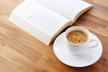 テーブルの上の開いたペーパーバック（洋書）と、コーヒーの入ったコーヒーカップで、コーヒーを飲みながらゆっくりと読書を楽しんでいるイメージ
