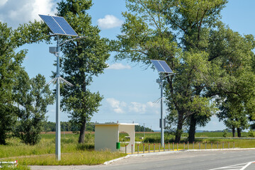 Bus stop with solar powered street lamps surrounded by tall trees and grass under a clear blue sky