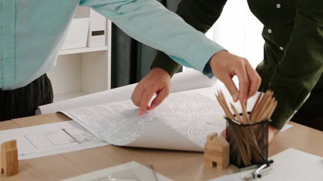 Smart architect and safety engineer discussion about building blueprint on table with architectural document, measurement tools and wooden block scatter around at modern office. Closeup. Delineation.