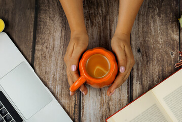 Cup of coffee in women's hands on wooden table I laptop and book, autumn mood
