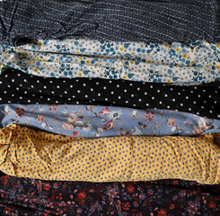 Photo of various printed fabrics. Arranged in horizontal stripes on background. Different colors and patterns. Floral prints, polka dots, ornaments. Blue, yellow, brown, white, black. Clothing. Folded