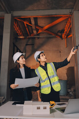 Construction manager and engineer dressed in orange work vests and hard helmets explore construction documentation on the building site near the steel frames