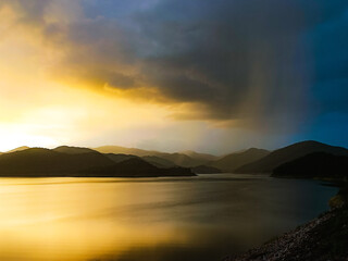 Fototapeta premium The last golden light at the horizon, before the raindrops fall upon the mountains.