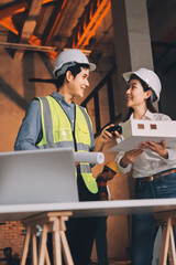 Construction manager and engineer dressed in orange work vests and hard helmets explore construction documentation on the building site near the steel frames