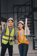 Construction manager and engineer dressed in orange work vests and hard helmets explore construction documentation on the building site near the steel frames
