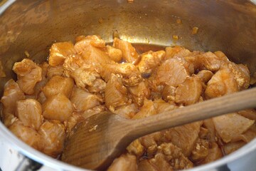 Chopped chicken breast pieces cooking as stew in a pot, close-up kitchen view.