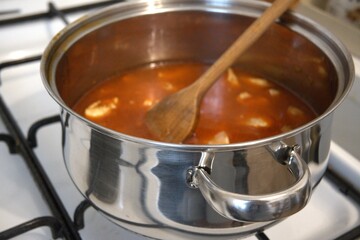 Chopped chicken breast pieces cooking as stew in a pot, close-up kitchen view.