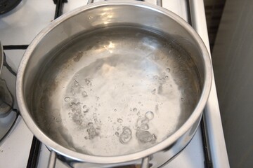Hot water bubbling in a pot on the stove, photographed in a kitchen, close-up view.