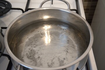 Hot water bubbling in a pot on the stove, photographed in a kitchen, close-up view.