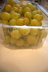 Fresh green grape bunch in a transparent plastic container, photographed close-up in a market or home setting.