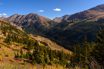 A winding road cuts through the valley on the way to Independence Pass, with majestic mountain ranges and a brilliant blue sky in the background.