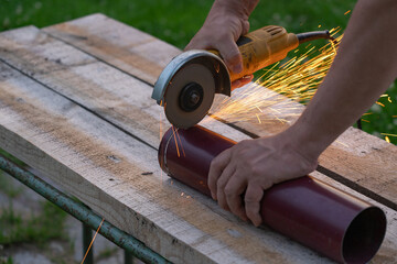 A man saws an iron pipe with a hand-held circular saw