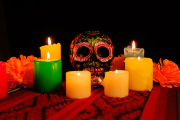 Black skull with vibrant floral decorations and candles for a Día de Muertos celebration