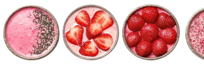 Four round bowls of pink smoothie topped with strawberries and seeds