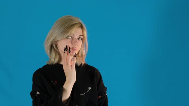 Young woman deep in thought lets fingers glide over cheek. Lady motion helps to process complex thoughts running through mind on blue background