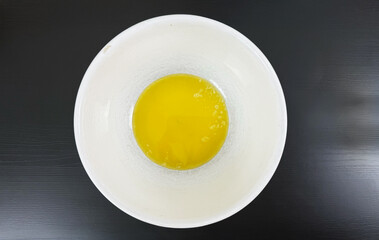 Melted butter in white mixing bowl on black background, captured from top view as an ingredient preparation step for chocolate chip cookie dough recipe