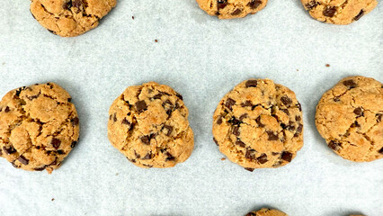 Multiple freshly baked chocolate chip cookies arranged on parchment paper, just out of oven during final stage of chocolate chip cookie preparation process