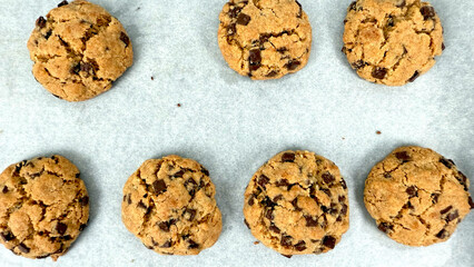 Multiple freshly baked chocolate chip cookies arranged on parchment paper, just out of oven during final stage of chocolate chip cookie preparation process