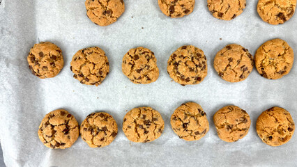 Multiple freshly baked chocolate chip cookies arranged on parchment paper, just out of oven during final stage of chocolate chip cookie preparation process