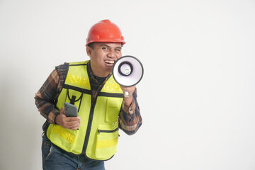 Asian construction worker wearing safety vest and helmet, holding a smartphone while speaking through a megaphone, delivering a promotional message with energy and confidence