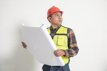Asian construction worker wearing safety vest and helmet, unfolding a large project paper plan. Isolated image on white background