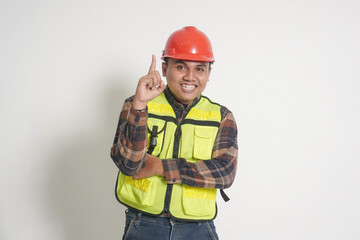 Asian construction worker wearing safety vest and helmet pointing up his forefinger and reminding something to do. Isolated image on white background