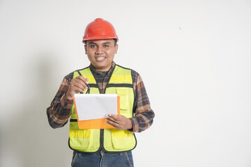Asian construction worker wearing safety vest and helmet, holding a clipboard while pointing and writing. Isolated image on white background