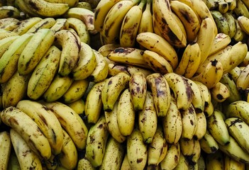 Close-up shot of a large pile of ripe yellow bananas on a market stall. The bananas are arranged in...