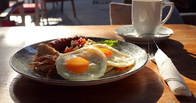 Plate with big Serbian breakfast meal at outdoor table in sunny morning, nutritious and tasty food served at downtown restaurant. Camera move around, showing close up view of eggs in bright backlight