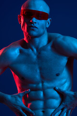 Athletic man posing confidently with sunglasses, showcasing his toned physique in vibrant blue and red lighting. A striking black and white aesthetic enhances the impact.