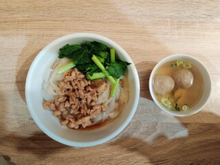 A top-down shot of a bowl of noodles with minced chicken and vegetables, served with a side bowl of bakso meatballs in clear broth