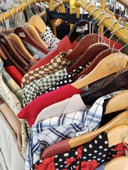 A tightly packed clothing rack displays a wide assortment of vintage and modern garments on wooden hangers, featuring various colors and patterns