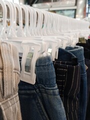 A long row of clothing on white plastic hangers, showing a selection of pants and skirts in various denim and fabric styles