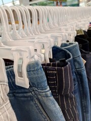 A long row of clothing on white plastic hangers, showing a selection of pants and skirts in various denim and fabric styles