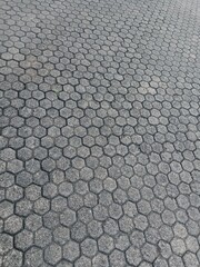A wide-angle, high-angle shot of a gray cobblestone path composed of interlocking hexagonal pavers, with dirt and sand filling the gaps.