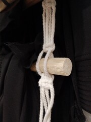A close-up shot of a white macrame knot hanging from a wooden dowel, against a blurry black background