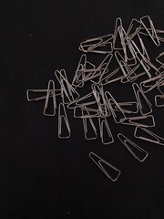 A chaotic pile of silver metal paper clips, scattered across a dark, textured background