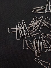 A chaotic pile of silver metal paper clips, scattered across a dark, textured background