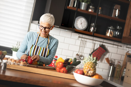happy senior woman chopping vegetables at her kitchen - Powered by Adobe