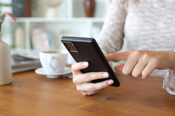 Woman hand browsing on cell phone on wooden table