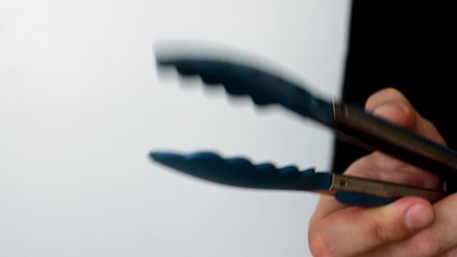 Chef with kitchen tongs in hands on white background.
Kitchen tongs for hot food.
Kitchen tools.
Kitchen attributes in a restaurant