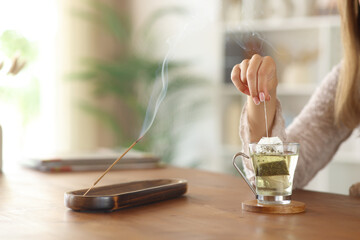 Woman hand preparing tea beside incense stick burning at home