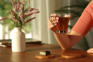 Close up of woman hand holding tea cup at sunset at home