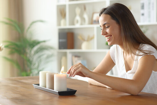 Happy woman lighting aromatic candles on a table at home - Powered by Adobe