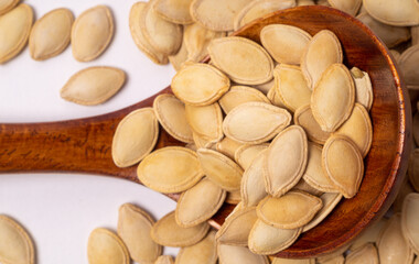 Pumpkin seeds in a wooden spoon close-up on a white background, top view, copy space