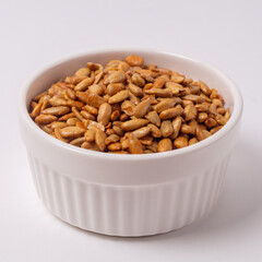 Peeled sunflower seeds in teriyaki sauce in a round plate on white background, side view