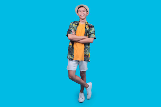 Smiling Young Man Standing Confidently With Crossed Arms And Legs On A Blue Background