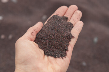 Close-up view of dark industrial sand from Jussaro Island, Finland, held in the palm of a hand. The iron-rich grains reflect the mining history and its unique, man-shaped shoreline