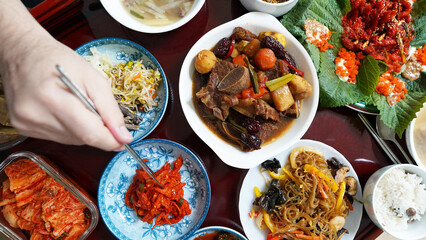 Korean Traditional New Year’s Feast with Braised Short Ribs, Japchae, Kimchi, Vegetables, and Hand Holding Chopsticks
